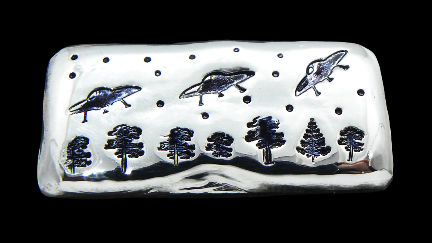 A 50g hand-poured fine silver bar featuring three UFOs, trees, trees and stars stamped images. The high-polish finish and soft edges highlight its handcrafted quality, while the dark patina enhances contrast and detail. A premium collectible from the Tasmanian Bullion Company.