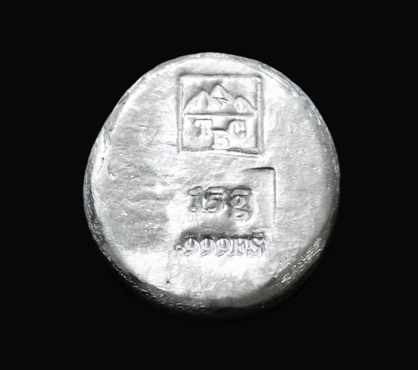 Underside view of a 15g hand-poured fine round silver bar, featuring our square TBC makers mark stamp on a smooth surface without patina and the 15g .999FS stamp. The reflective finish highlights its handcrafted quality and unique pouring texture, making it a premium bullion piece from the Tasmanian Bullion Company.